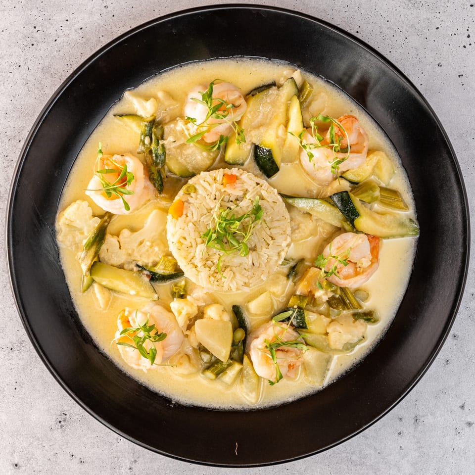 Overhead view of a creamy shrimp and vegetable dish with a mound of rice in a black bowl.
