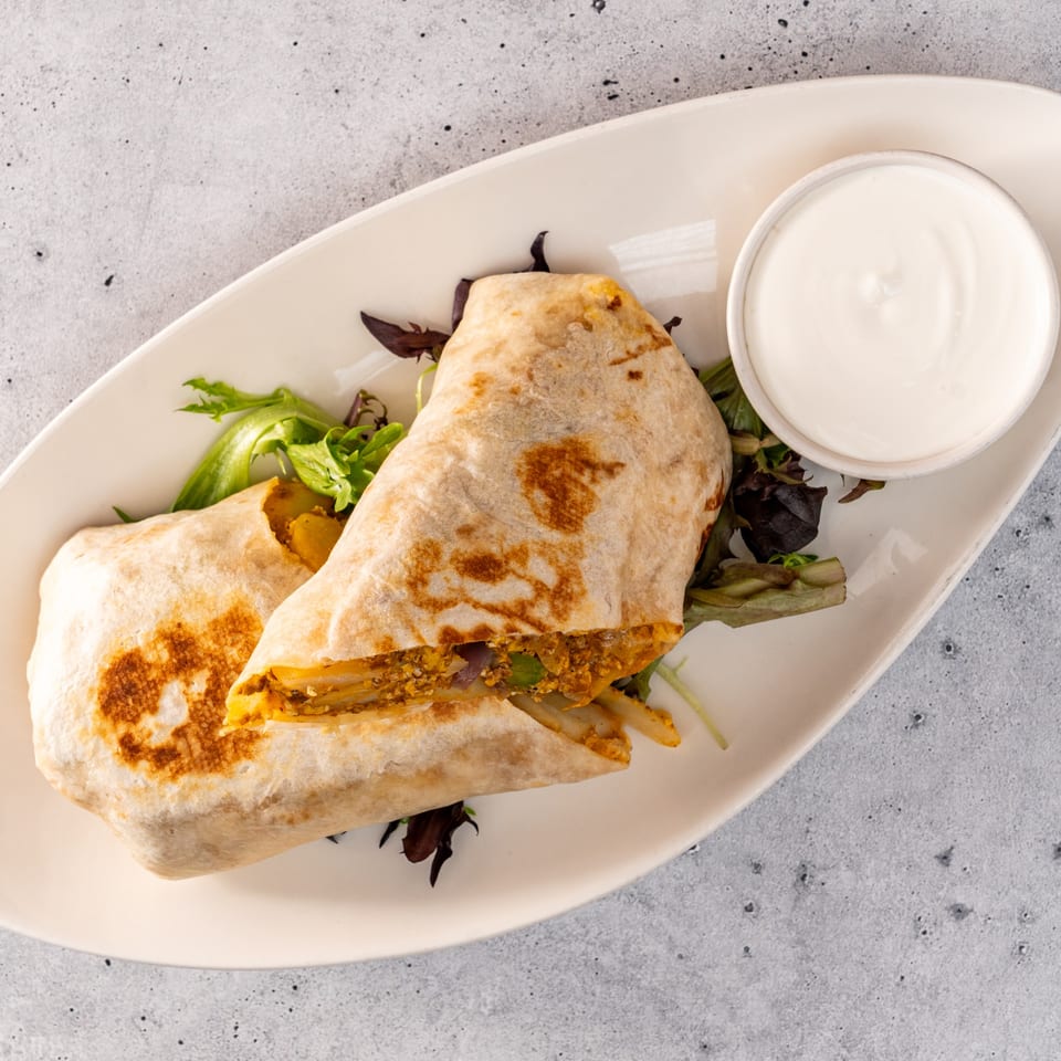 Two Raices Cocina & Bar burritos with a side of sour cream on a white plate.