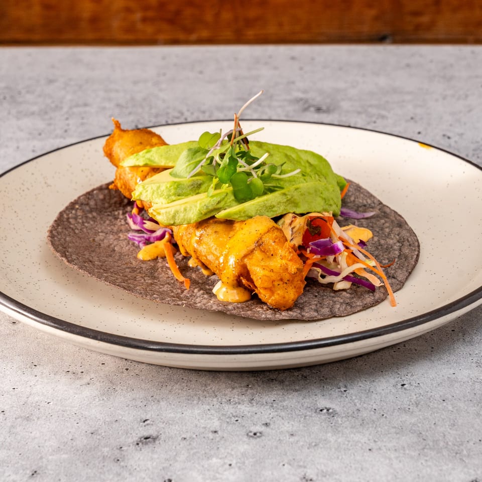 Raices Cocina & Bar's fish taco with avocado, slaw, and sauce on a blue corn tortilla.