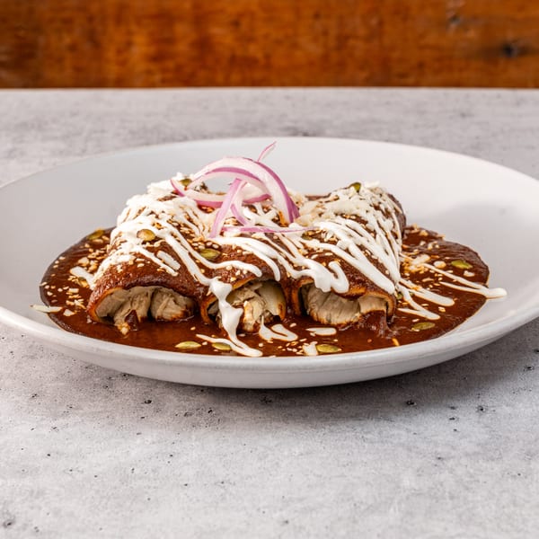 Three chicken enchiladas covered in rich mole sauce, crema, sesame seeds, and red onion slices.
