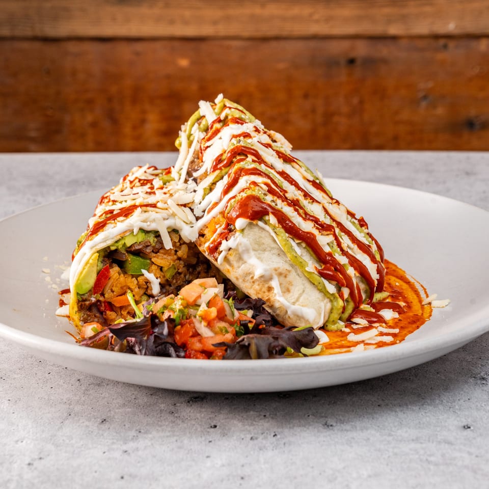 A large, sauced burrito with rice, meat, and avocado, served with pico de gallo.