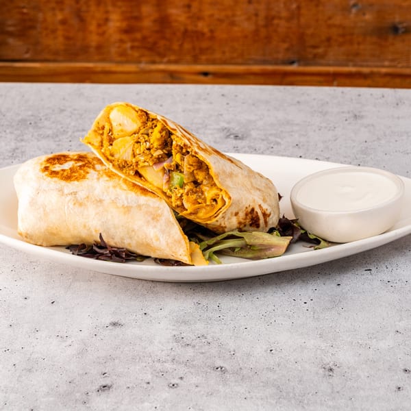 A Raices Cocina & Bar burrito, cut in half, revealing a savory filling, served with sour cream.
