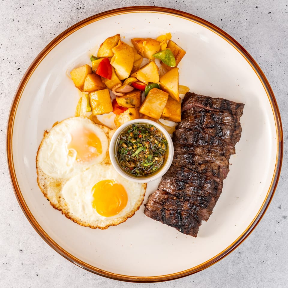 Grilled skirt steak, two fried eggs, roasted potatoes with bell peppers, and a side of salsa.