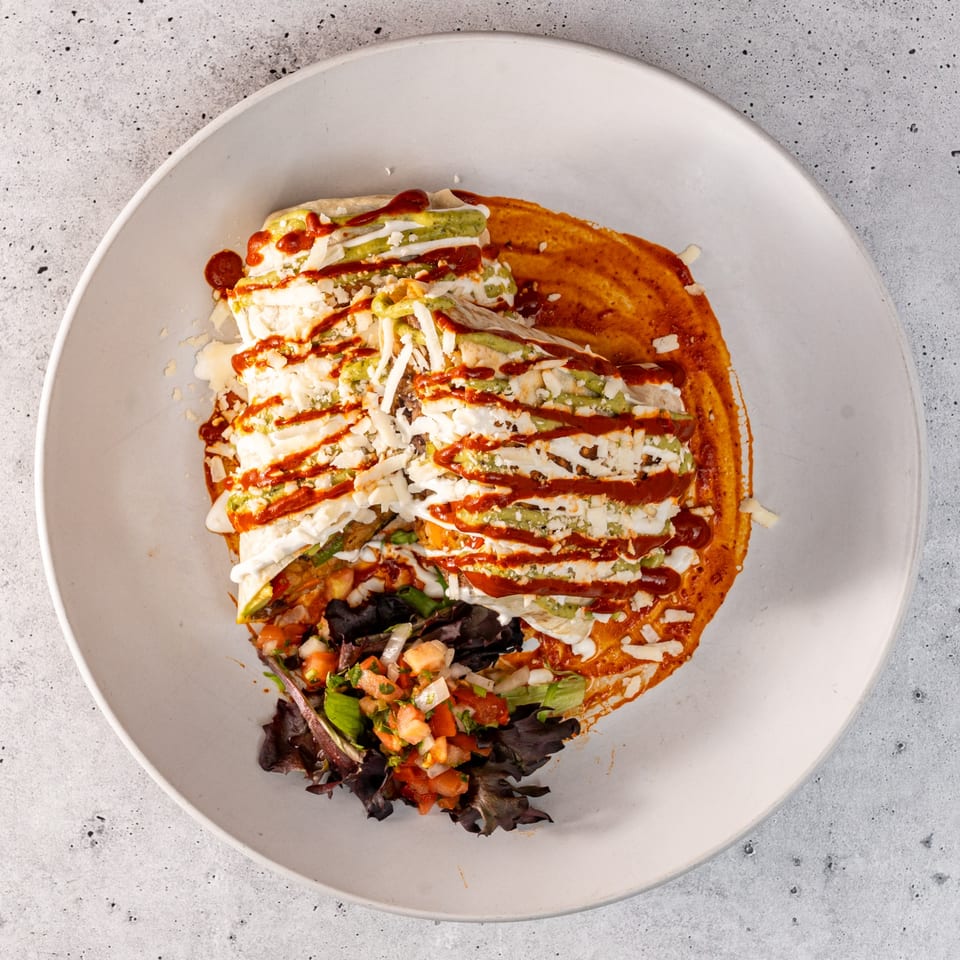 Mexican enchiladas with red sauce, green sauce, white cheese, and pico de gallo on a white plate.